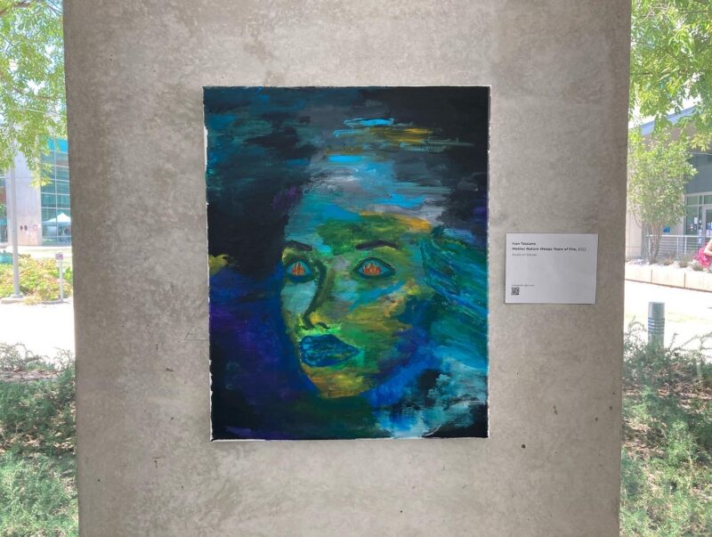 A canvas painting of a green and blue woman, or Mother Nature, with flames reflecting in her eyes.
