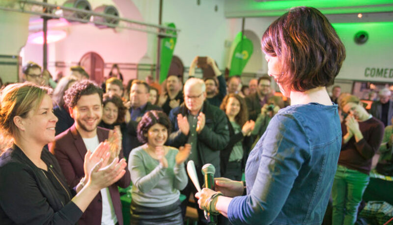 Annalena Baerbock speaks at a Green Party event. A small crowd is applauding her.
