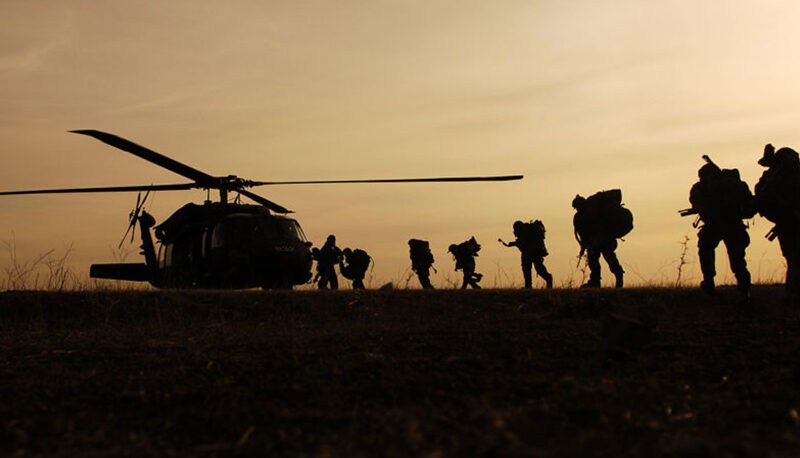 The Israel Defense Forces silhouetted against an orange sky headed toward a helicopter.