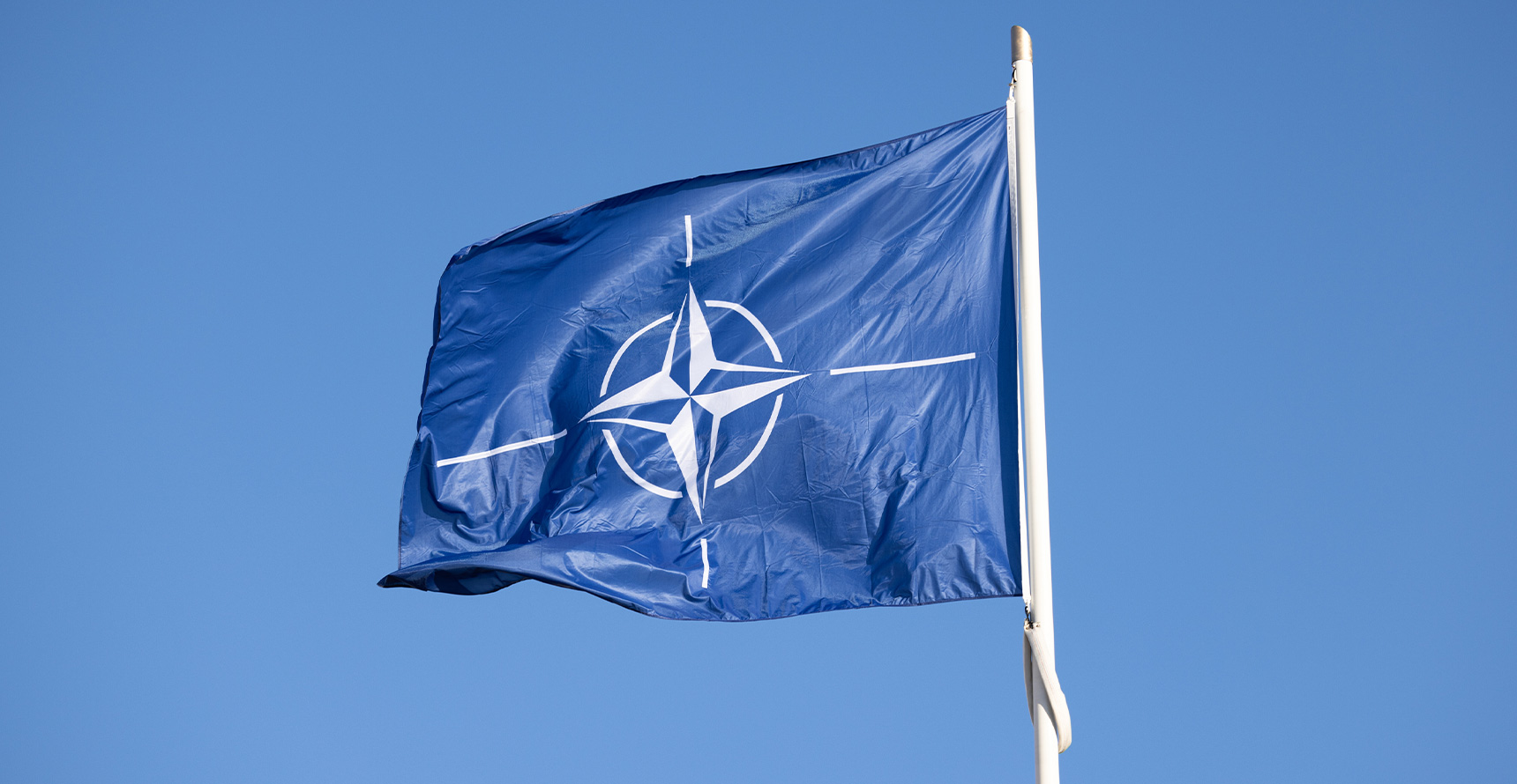 The NATO flag against a clear blue sky.