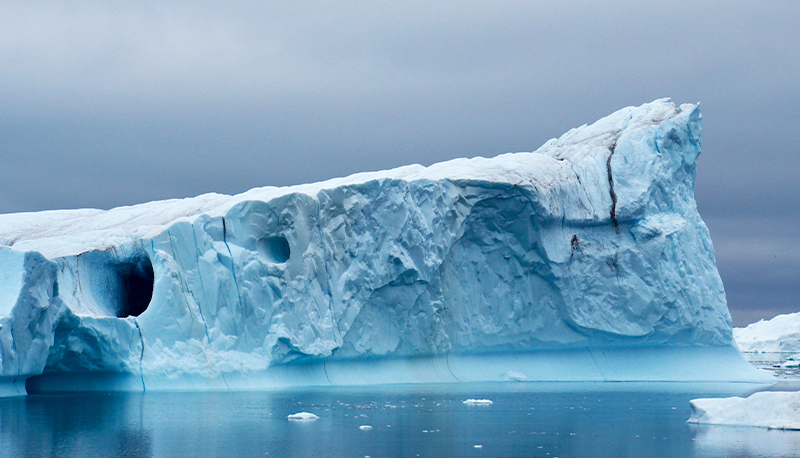 An iceberg against a gray sky and blue ocean.