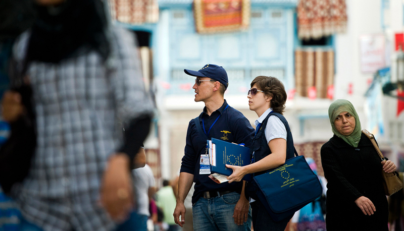 EU Election Observation Mission in Tunisia. A man and a woman in a busy square holding blue folders with the European Union symbol on the front.