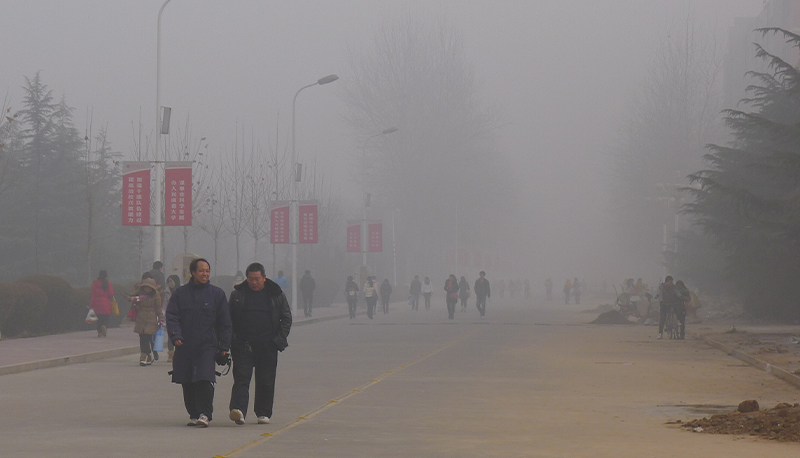Two men walking through gray, polluted air in Henan Province, China.