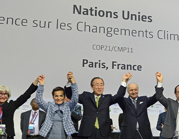 A group of world leaders at COP 21 after the signing of the Paris Agreement. They are holding their joined hands in the air in triumph against a white background.