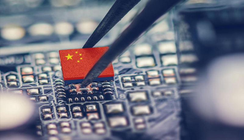 Close-up photo of a microchip being added to a circuit board. The microchip bears the image of the Chinese flag.