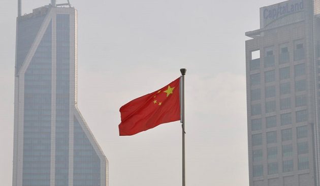 Chinese flag flying in foreground. High-rise buildings in background.