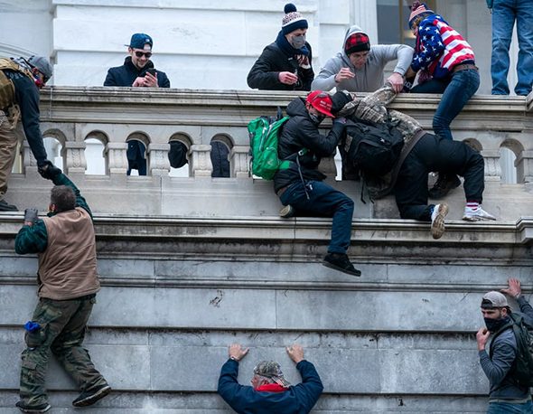 Insurrectionists scale a wall outside the US Capitol building during the January 6th attacks