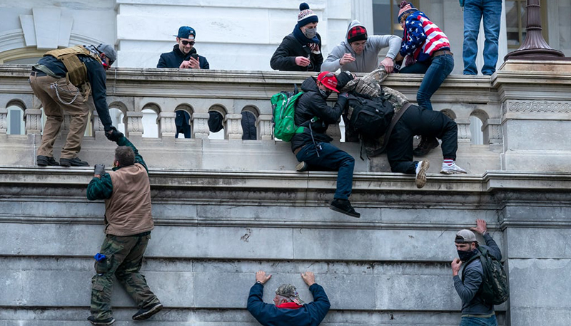 Insurrectionists scale a wall outside the US Capitol building during the January 6th attacks