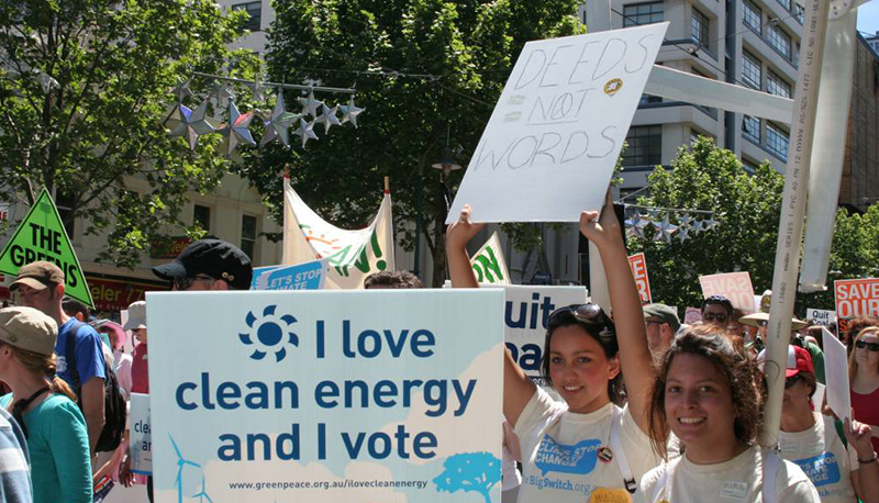 Greenpeace activists march against global warming, holding signs that read "I love clean energy and I vote" and "Deeds not words"