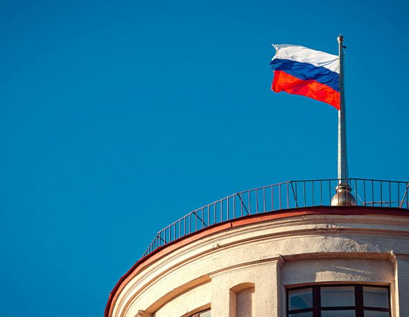 Photo of a Russian flag flying above a building in front of a blue sky