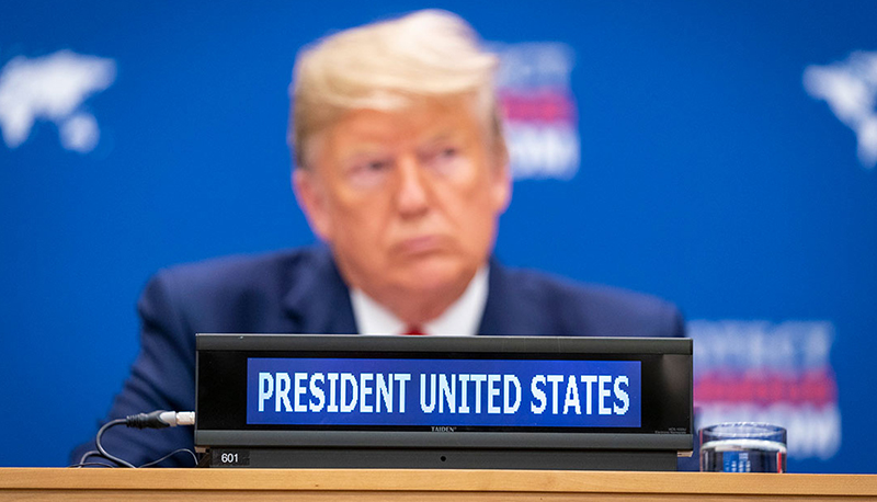Donald Trump sitting behind a nameplate that reads "President United States"