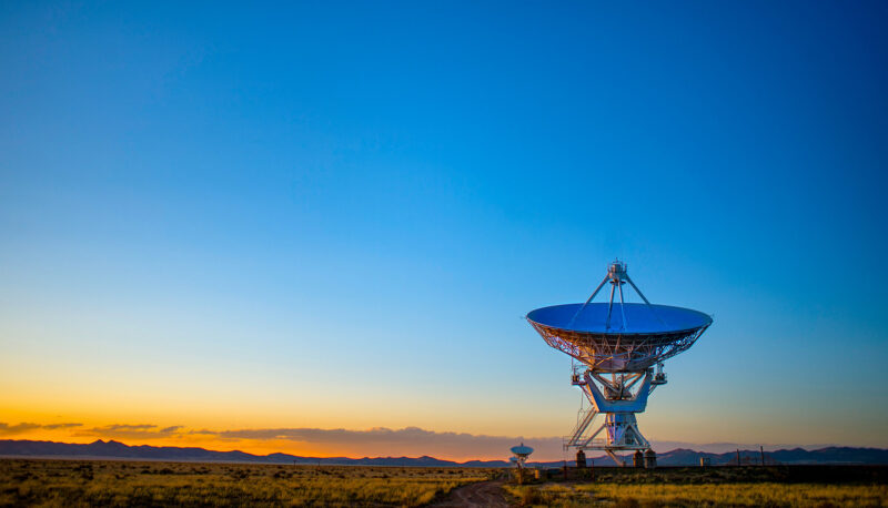 A satellite dish in a desert landscape at sunrise