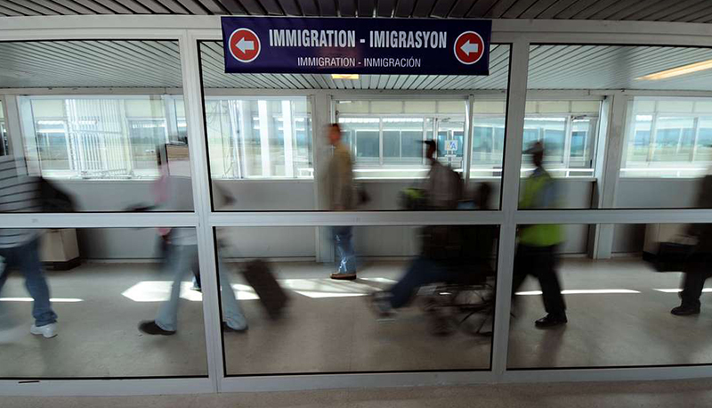Airport passengers walk through a terminal with signs labeled "Immigration"