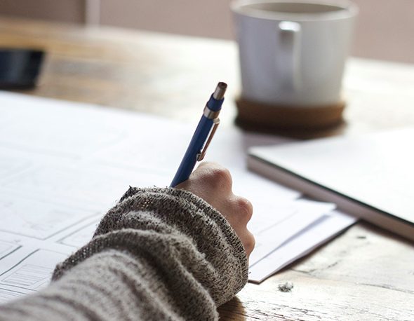 Close-up photo of a person writing on a blank piece of paper with a mug nearby