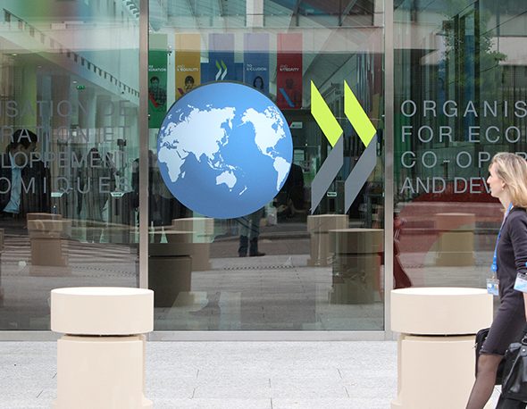 Two women walk on the sidewalk in front of the OECD conference building in Paris