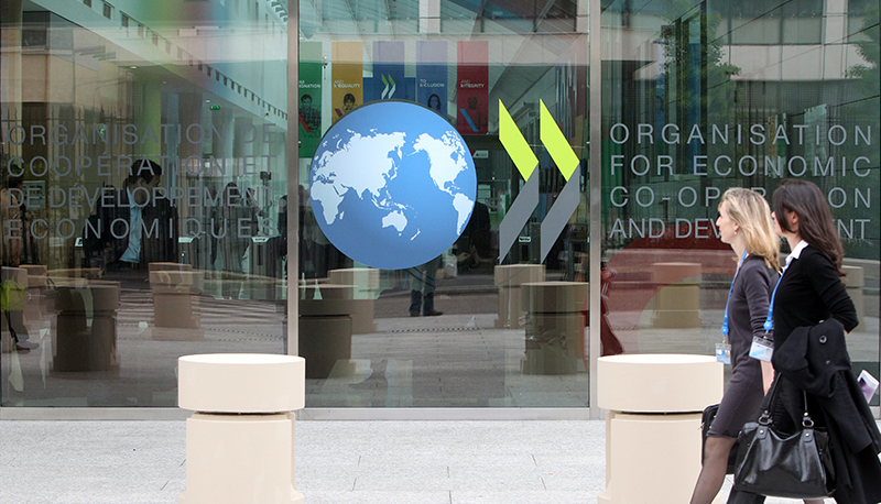 Two women walk on the sidewalk in front of the OECD conference building in Paris