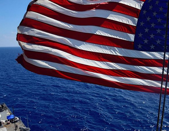 An American flag waves above a U.S. Navy ship
