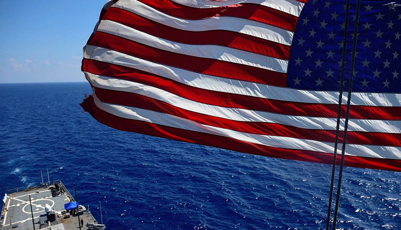 An American flag waves above a U.S. Navy ship