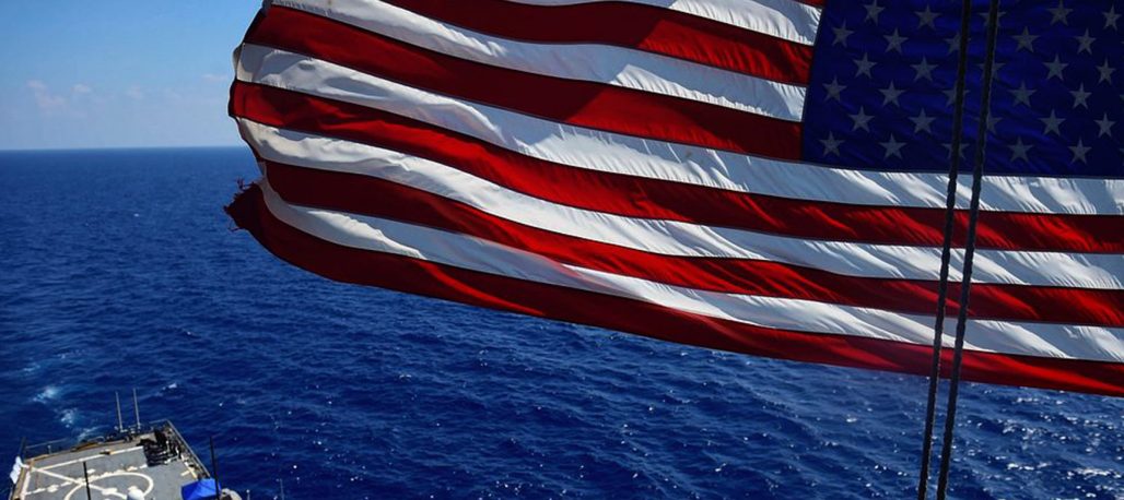An American flag flies above a U.S. Navy ship at sea