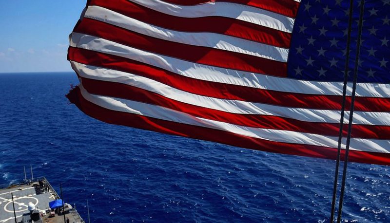 An American flag flies above a U.S. Navy ship at sea
