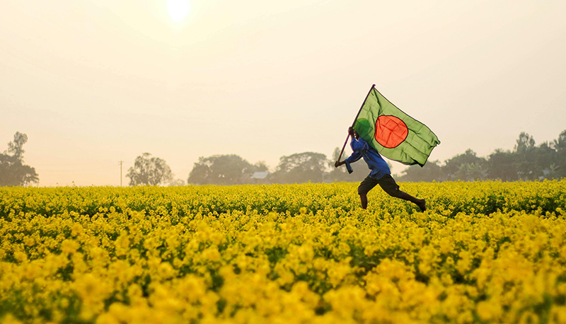 Photo shows a person holding the Bangladesh flag running through a field.