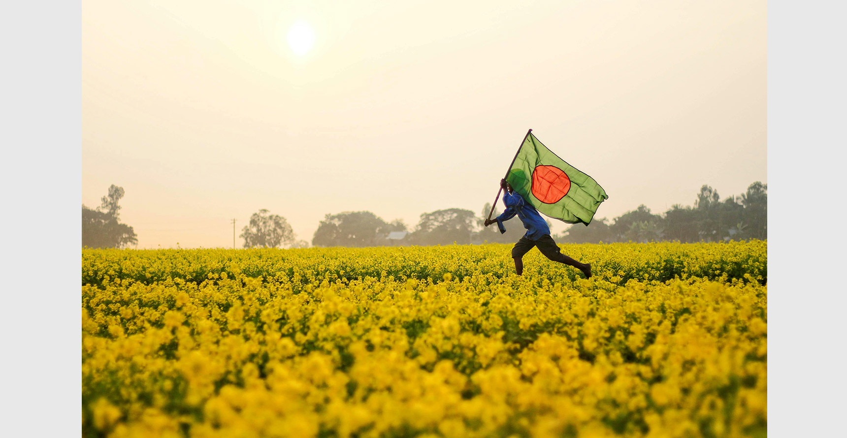 Photo of a man carrying a Bangladesh flag running through a field.