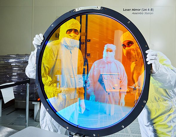 Lawrence Livermore National Laboratory optical engineers Justin Wolfe (left) and Simon Cohen hold up the r filter for Vera C. Rubin Observatory’s LSSTCam. Assembly technician Frank Arredondo appears in the filter’s reflection.