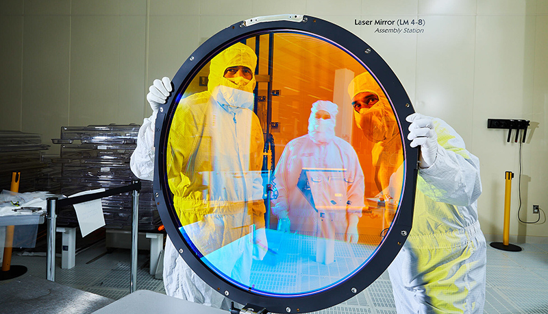 Lawrence Livermore National Laboratory optical engineers Justin Wolfe (left) and Simon Cohen hold up the r filter for Vera C. Rubin Observatory’s LSSTCam. Assembly technician Frank Arredondo appears in the filter’s reflection.