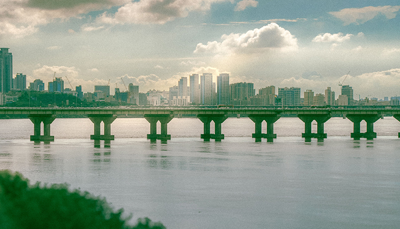 View of Seoul's skyline with a bridge spanning the Han River under a cloudy sky.