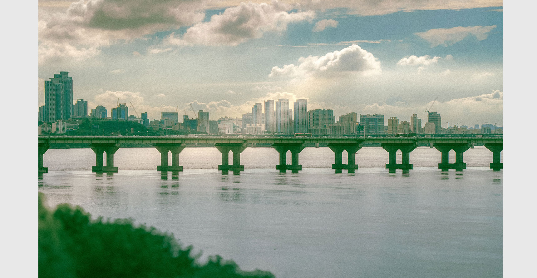 View of Seoul's skyline with a bridge spanning the Han River under a cloudy sky.