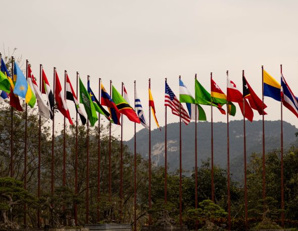 A display of various national flags on flagpoles set against a mountain backdrop, symbolizing global unity.