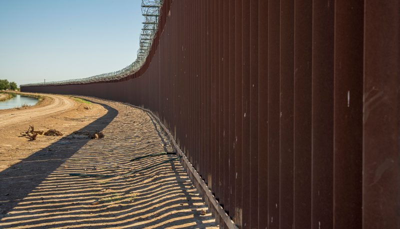 Long view of a steel border wall under clear skies.